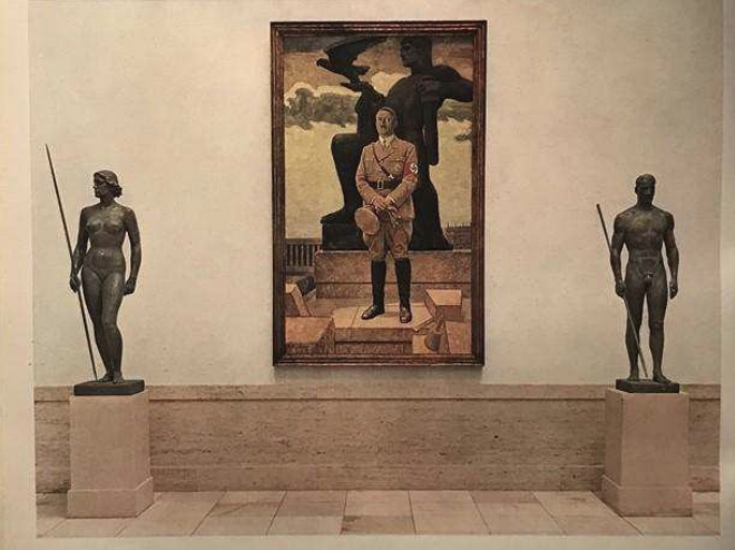 Museum mit zwei Bronzestatuen links und rechts, dazwischen großes Bild eines uniformierten Mannes mit Armbinde.